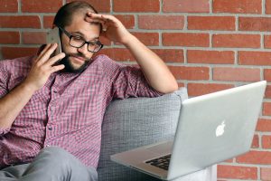 frustrated bearded man on cell phone gazing at laptop