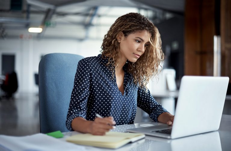 Cropped shot of a young businesswoman making notes while working on a laptop in a modern office